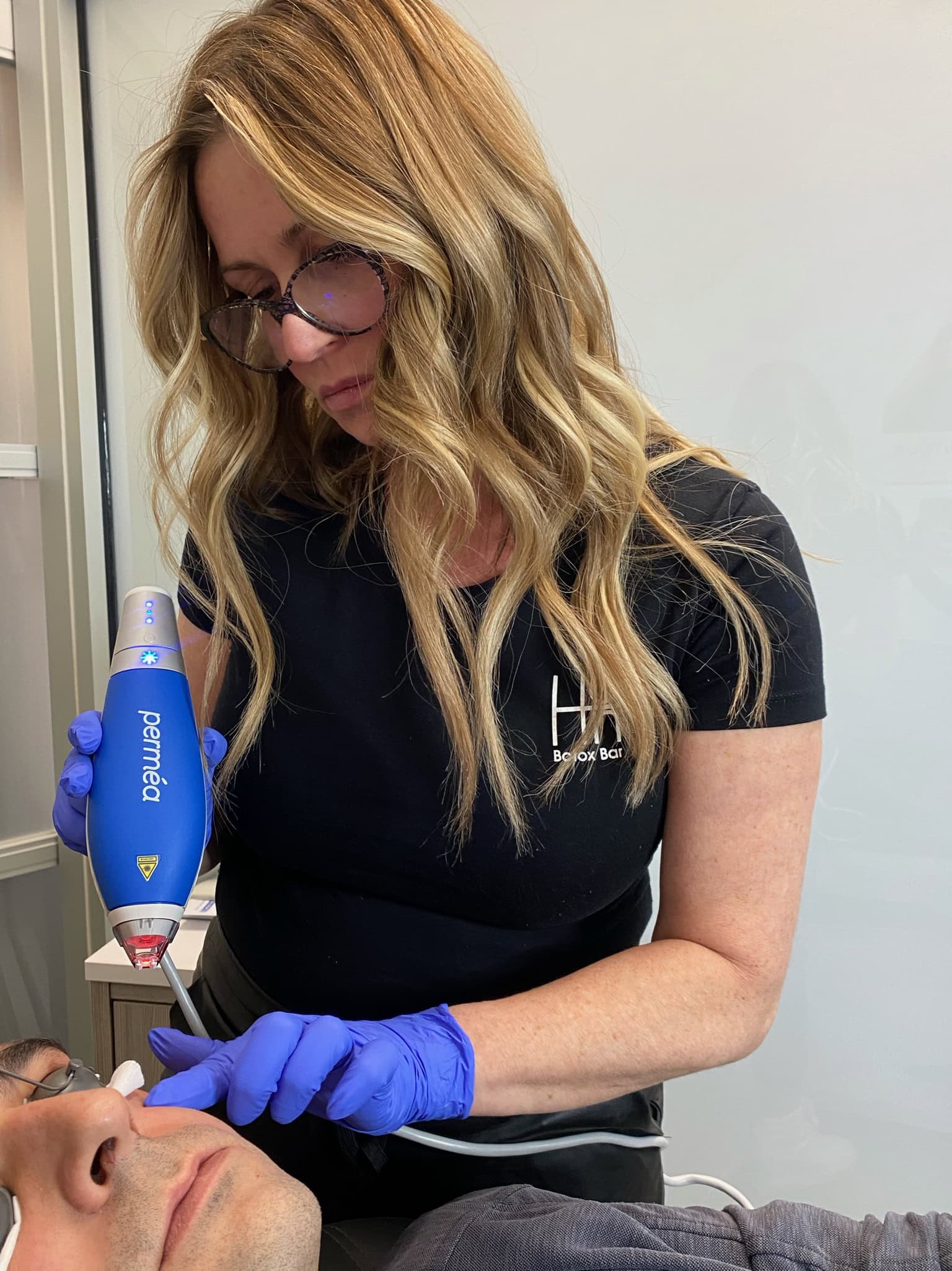 A woman in gloves uses a blue laser on a man's face, a treatment often paired with microneedling.