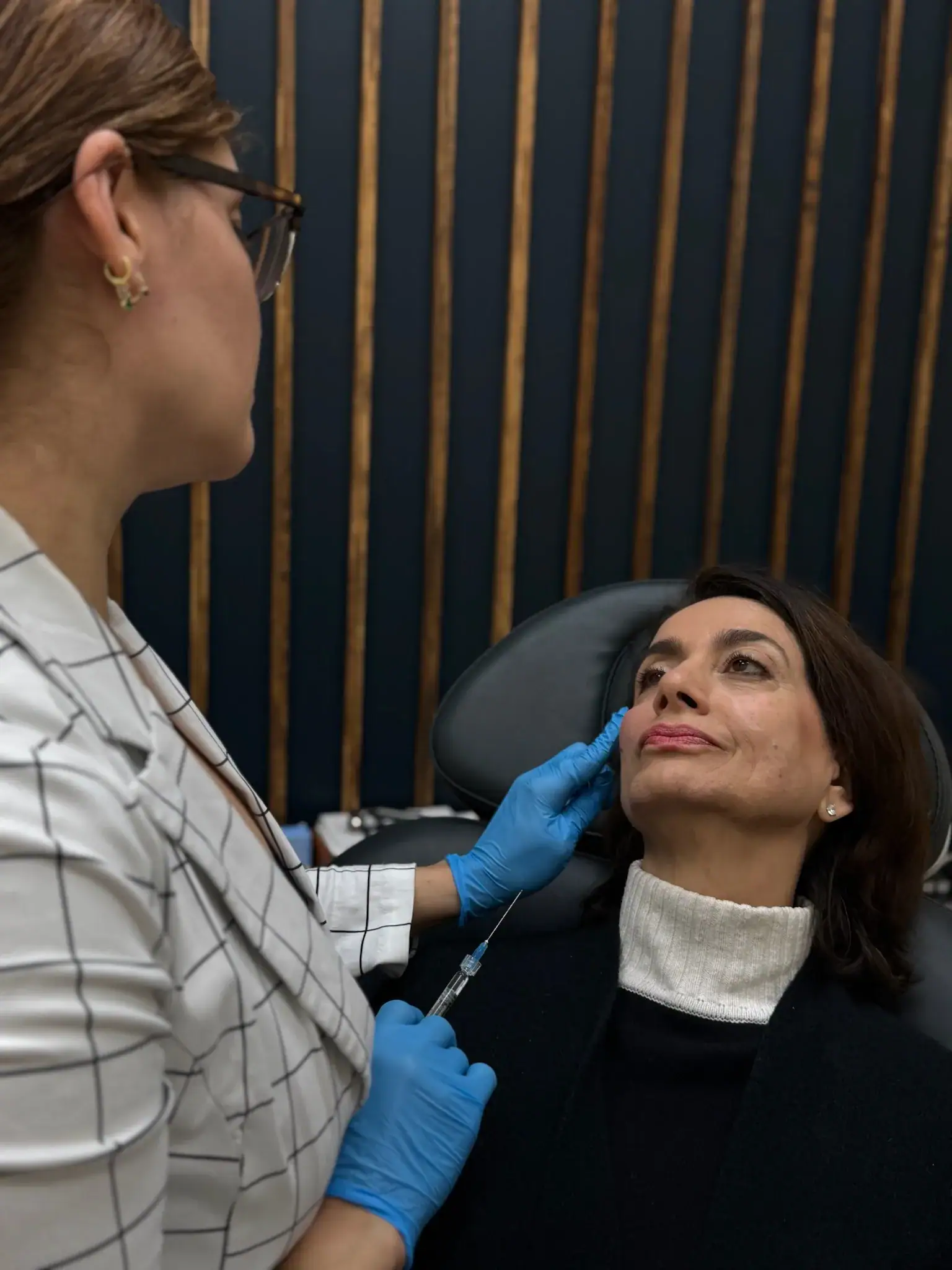 Cosmetic specialist giving a Botox injection to a seated woman.
