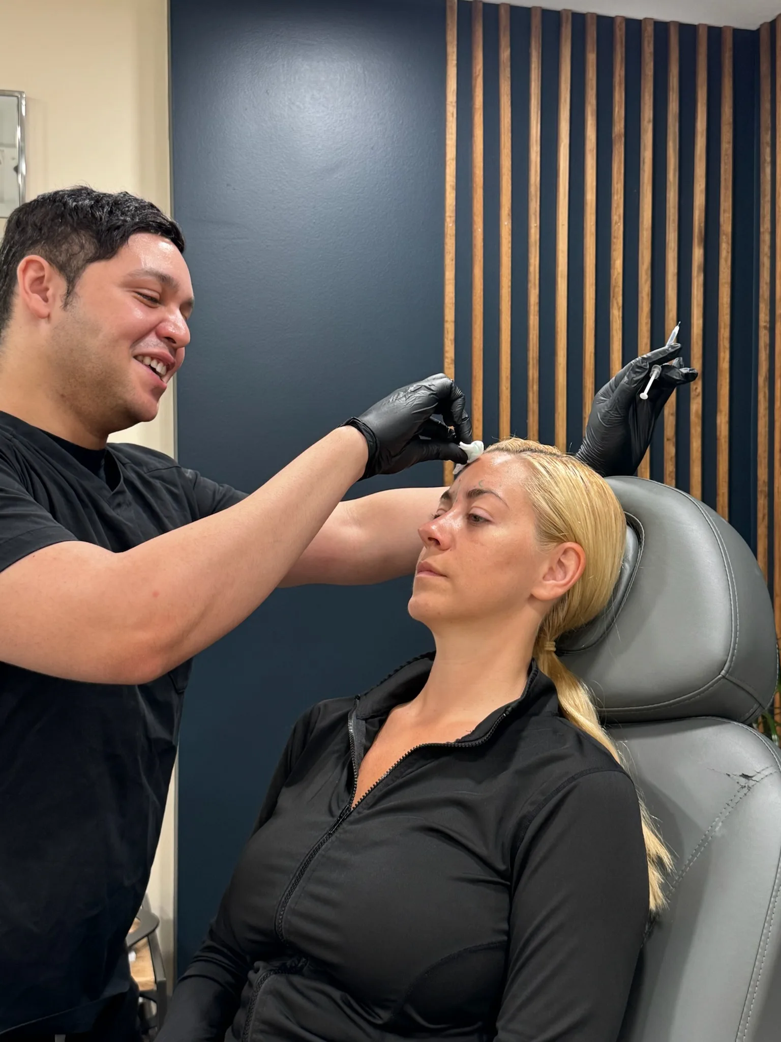 Professional administering cosmetic injection to woman's forehead at clinic