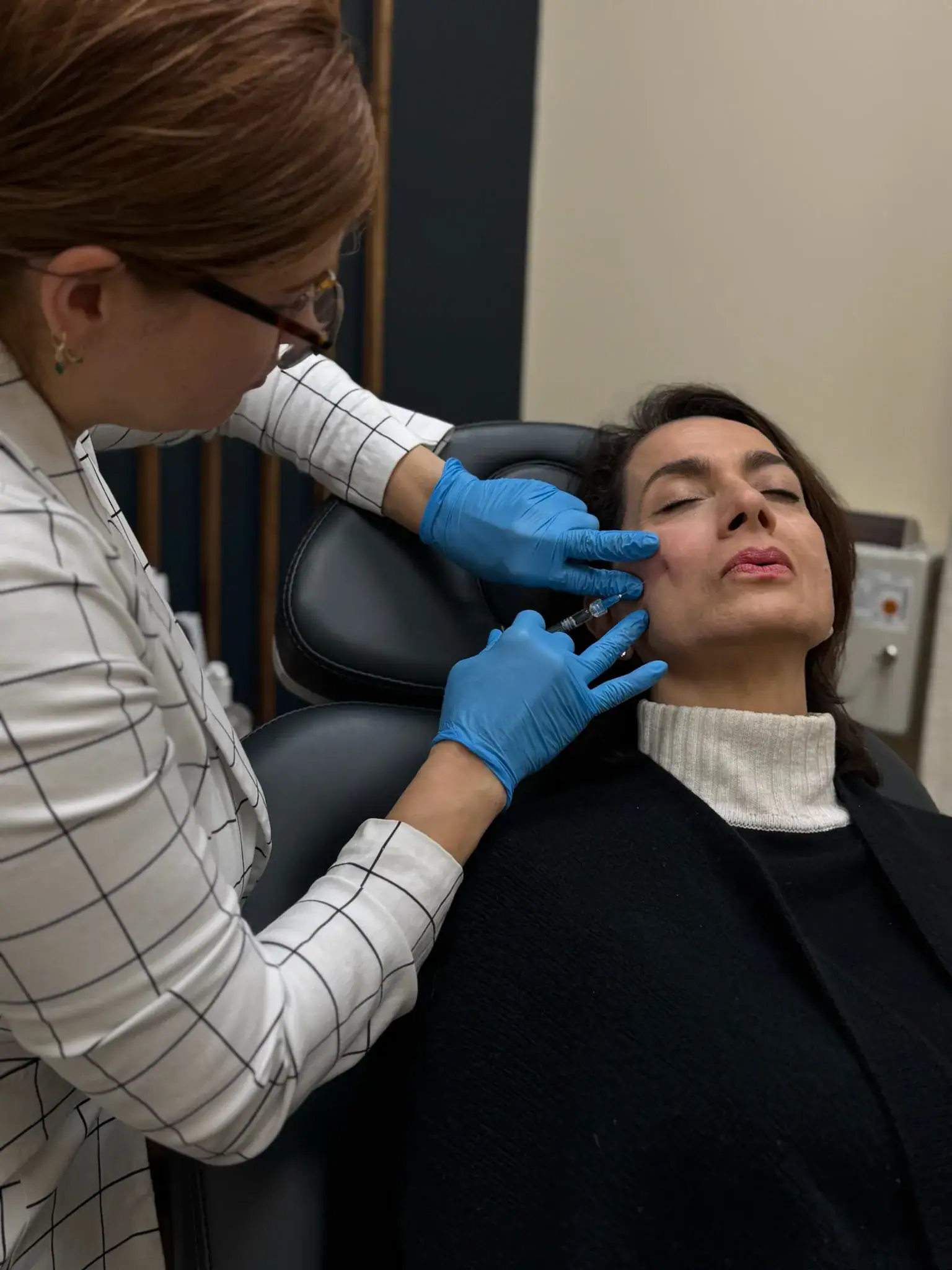 Aesthetician administering facial injection to woman in clinic.